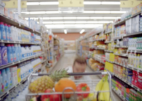 Justin Timberlake jumping on shopping cart in grocery store aisle.