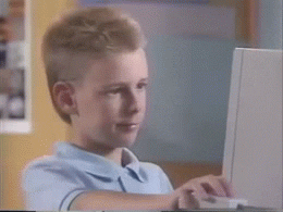 Um adolescente branco está mexendo em um computador, solta o mouse e faz um sinal de joinha com a mão.