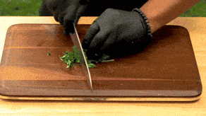 Hands chopping fresh parsley on a wooden cutting board with a chef's knife