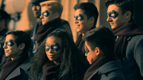 The Umbrella Academy as children, weazring domino masks. A flash flares from a press camera. One of the children (Ben) still has blood on his face from the mission.