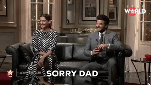 A brown woman in a black, white polka dotted dress says: "Sorry Dad" to her father next to her. He is a brown man in a gray suit.