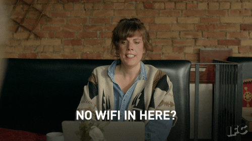 mulher sentada em uma sala perguntando em inglês "não tem wi-fi aqui?"