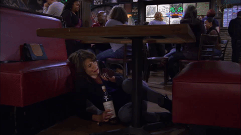 a gif of a woman drinking under a table