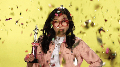 Giphy of Awkafina holding a trophy with confetti falling around her