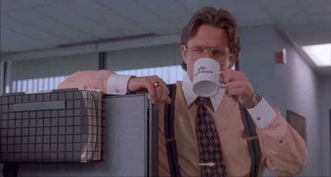 homem de roupa social e gravata, levando uma caneca até a boca enquanto encosta o braço em uma divisória de escritório