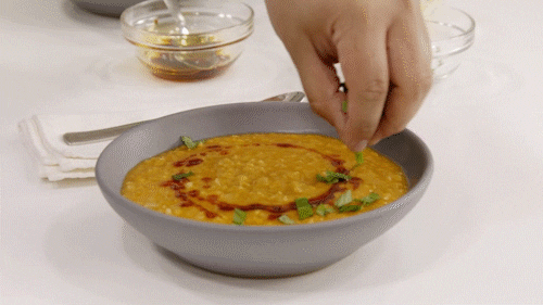 A hand garnishes a bowl of yellow daal (lentil).