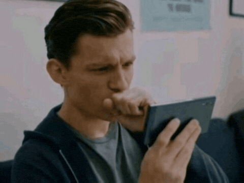 Man frowning and squinting at his phone screen with a hand over his mouth