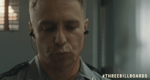 Sam Rockwell, a man in a military uniform wearing earphones, standing in front of three billboards