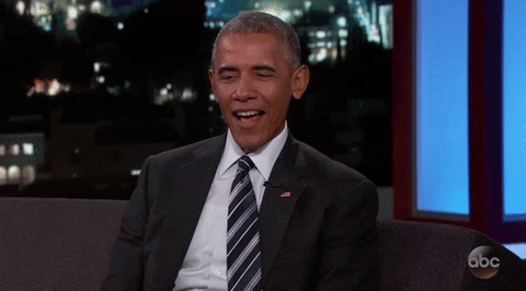 Barack Obama glimlacht en steekt zijn hand op tijdens een talkshow.