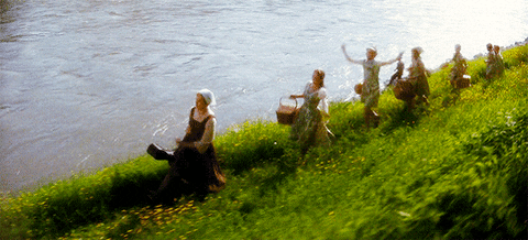 Women and children skip across the banks of a river with picnic baskets in their hands. 