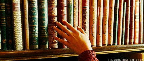 A hand goes over a shelf of books.