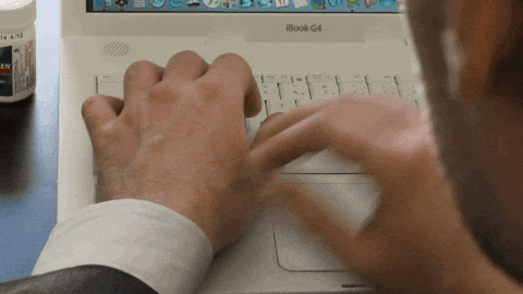 un hombre frente a u laptop revisando la hora en su reloj de mano.