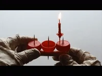 Gloved hands holding a row of red cups beside a lit candle