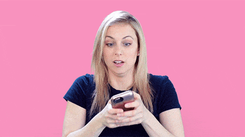 GIF of woman on a pink backdrop holds a phone in front of her as she texts with overt enthusiasm