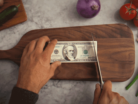 man cutting up a stack of money on a cutting board to signify components fo a social media marketing budget for small businesses