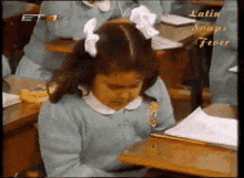A Quinceanera-themed GIF of a little girl sitting at a desk in a classroom