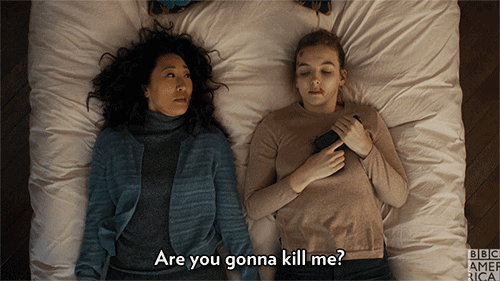 A gif of Eve and Villanelle lying in bed together, fully clothed. Villanelle cradles a gun and has a bloody lip. The caption says “Are you gonna kill me,” and represents lines spoken by Eve