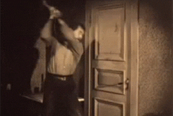 A black & white image of a man attacking a door handle with an axe.