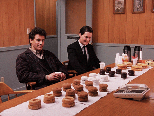 Agent Cooper and Sheriff Truman from Twin Peaks smile at stacks of donuts. 