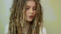 A woman with blonde dredloacks messily pulls her hair over to one side of her head