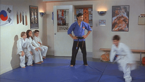 A master at a Taekwondo dojo giving a nod of approval to his adult student as he chases a kid