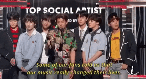 [Image description: All 7 members of BTS are pictured accepting their second Billboard Music Award. Their leader RM is giving a speech, saying, “Some of our fans told us that our music really changed their lives.”] Attribution: Giphy.com