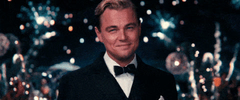The Great Gatsby: Leonardo DiCaprio in a tuxedo smiles, pleased, in front of fireworks