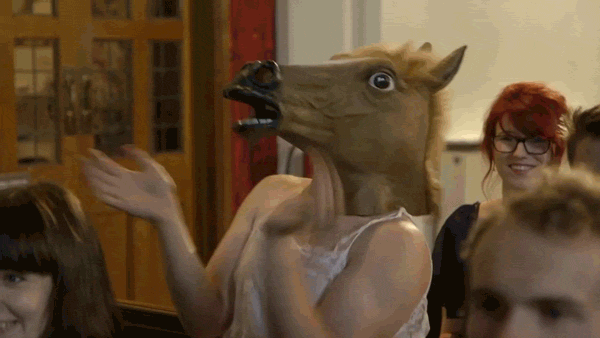 Woman clapping with a horse mask over her head and giving a thumbs up