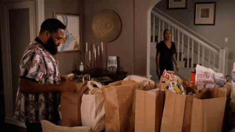 Hombre poniendo muchas bolsas de mandado mientras su esposa lo ve sorprendido