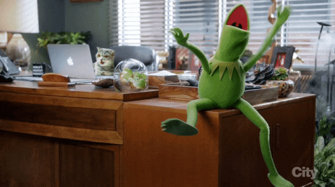 Kermit, o sapo, comemorando sentado em cima de uma escrivaninha.