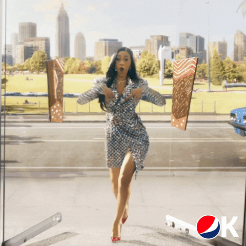 Cardi B wearing a a shiny outfit and walking towards the camera clapping for a Pepsi commercial.