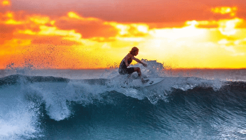 A statue still surfer on a wave that is moving against a sunset
