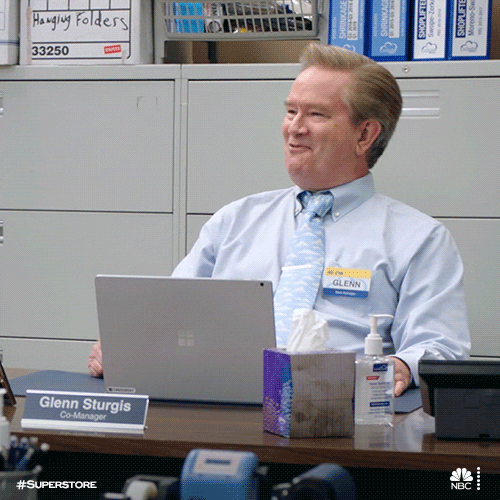 A GIF of Glenn from Superstore sitting at his desk with his laptop in front of him lifting his right arm in celebration.