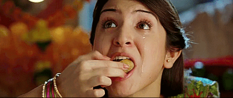  A dark-haired brown woman is crying as she stuffs food into her already-full mouth.