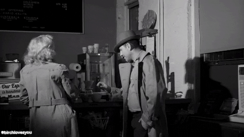 Cena de um filme antigo mostra duas pessoas brindando com xícaras de café