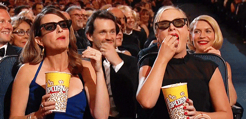 Tina Fey e Amy Poehler comendo pipoca e usando óculos 3D na arquibancada de uma premiação de cinema