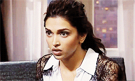 A brown woman in a black-and-white shirt looks around confused.