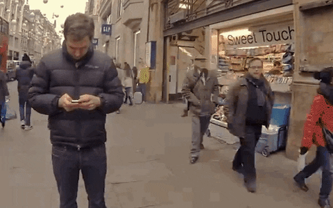 GIF de um homem olhando o celular no meio da rua