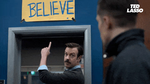 Ted Lasso: Ted turns around in a locker room and points up at a yellow sign that reads Believe