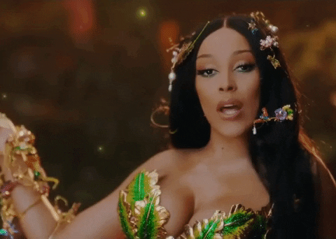 Gif of Doja Cat singing. She has flower hairpins in her hair and a dress of green leaves with gilding.