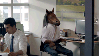 Office worker wearing a horse mask turns in his chair while shaking his head