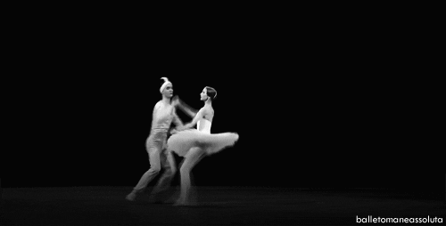 Two ballet dancers dance in black and white. The man holds the girl's hand while she jumps and lands to go directly into a relevé with her leg pointed up. 