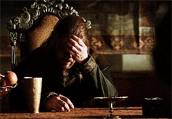 Ned Stark from Game of thrones is sat in a chair, looking exasperated as he puts his hand to his forehead