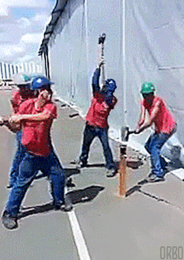 Four construction workers hitting a pole with sledgehammers in a staggered rhythm