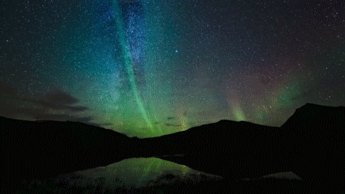 Moving image of the green and red northern lights over a lake and mountains. 