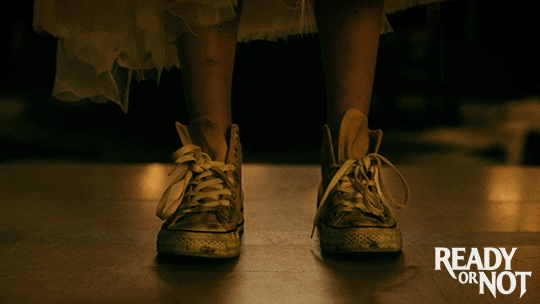 Panning shot of Grace (Samara Weaving), from her converse-clad feet and tattered wedding-dress, up through her rifle and ammunition, to her stunned and grim face