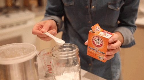 woman putting a spoon of baking soda in a jar