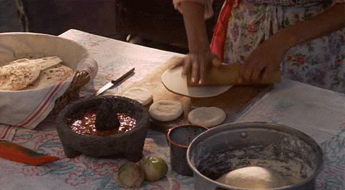 A woman in a kitchen preparing food on a table, showcasing the art of making tortillas in Mexican cuisine during a Quinceanera celebration.