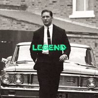 Man in a suit by a vintage car, captioned legend