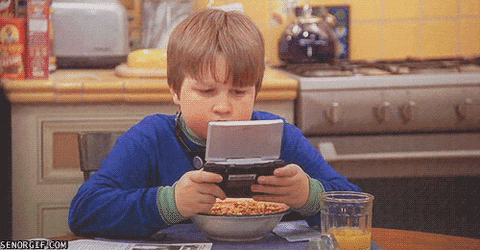 boy plays gameboy and eats cereal